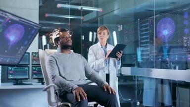 男子穿着脑波扫描耳机坐在椅子上, 而科学家与平板电脑监督过程。现代脑研究中的实验室监测显示<strong>英语阅读</strong>和脑模型.